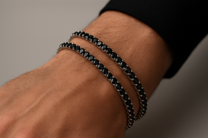 Vyriška ranka su dviem tennis apyrankėmis iš balto aukso, inkrustuotomis juodais deimantais.