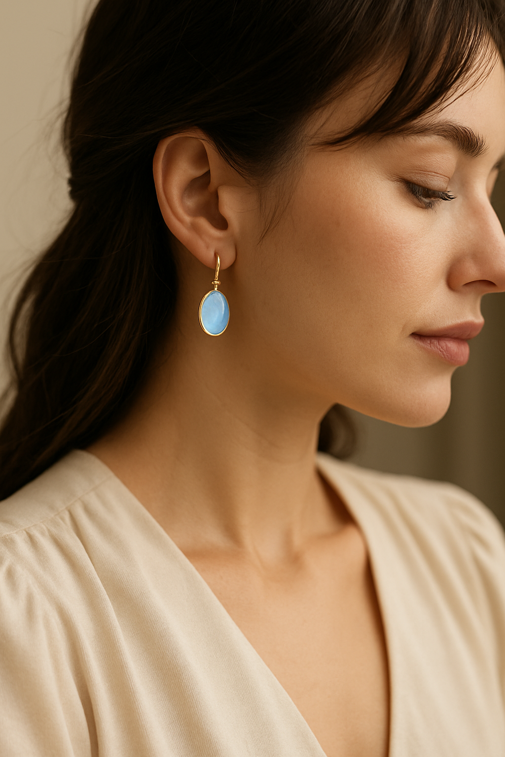 Stilingos moters profilis su kabančiais ovalo formos balto mėnulio akmens auskarais, elegantiškas papuošalas prie švelnios palaidinės.