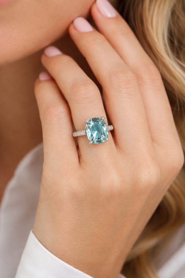 Balto aukso sužadėtuvių žiedas su dideliu cushion formos akvamarinu, kurio atspalviai nuo žalsvai mėlynos iki giliai jūros mėlynos