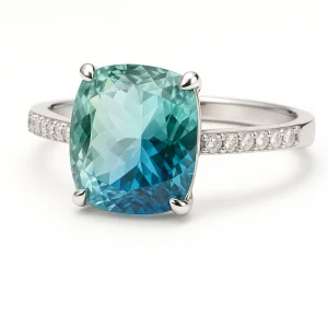 Balto aukso sužadėtuvių žiedas su dideliu cushion formos akvamarinu, kurio atspalviai svyruoja nuo žalsvai mėlynos iki šviesiai ar giliai jūros mėlynos, su subtiliais deimantais