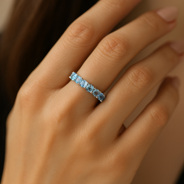 Stilingos moters ranka su žiedu juostele iš balto aukso, inkrustuotu šviesiai mėlynais akvamarinais ir deimantais, atspindinčiais vandens žvilgesį