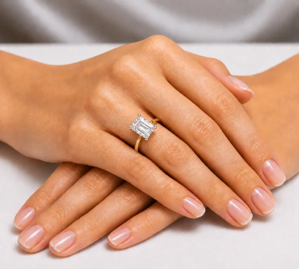 Sužadėtuvių žiedas su Emerald deimantu (Lab Grown 2.00 ct) geltonas auksas ant merginos rankos
